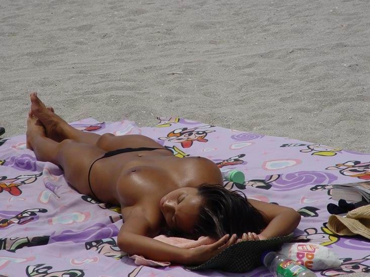 Голая девушка на пляже загорает под солнцем 