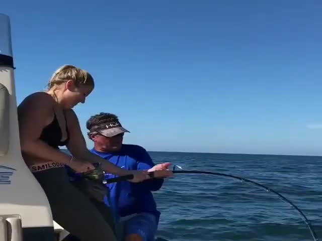 Девушка пытается вытянуть из воды огромную рыбу