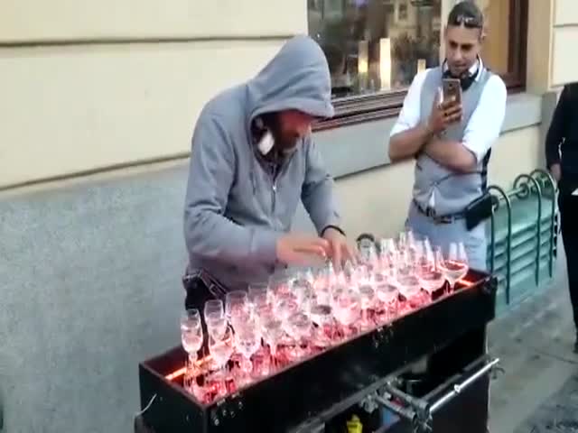 Уличный музыкант играет мелодию с помощью бокалов с водой