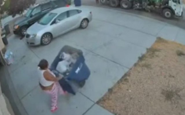 Женщина пытается совладать с мусорным контейнером